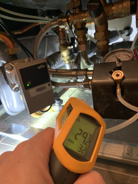 IR-termometer som visar 20.9° C riktad mot rör med en cirkulationspump i bakgrunden.