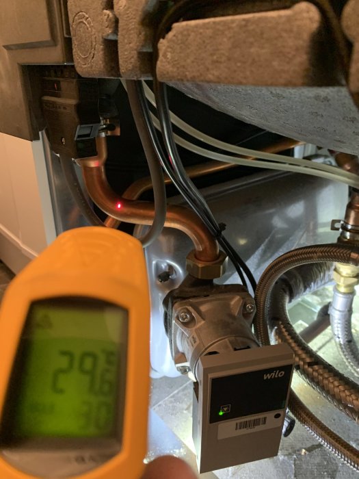 IR-termometer visar 29.6°C riktad mot isolerade rör och en Wilo cirkulationspump i ett pannrum.