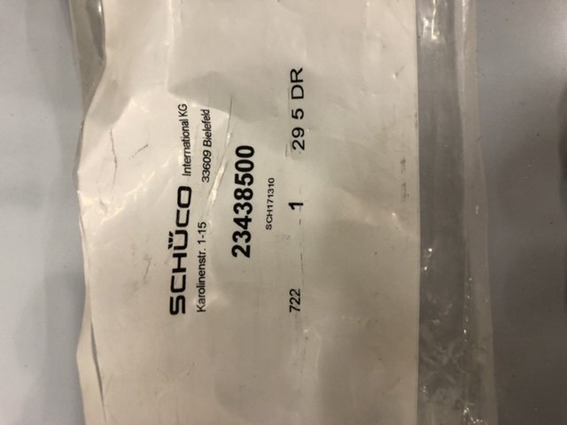 Etikett från SCHÜCO med artikelnummer 23483500, genomskinlig plastförpackning, suddig bakgrund.