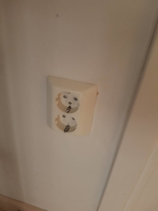 En sladd går från en dubbeluttag i en vit vägg in i ett annat rum.