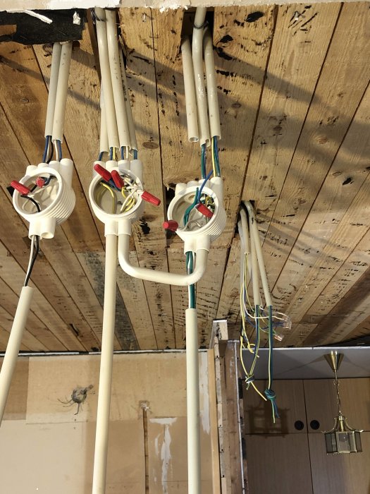 Råsponttak med borttagna brädor som exponerar elinstallation med plastkanaler och eldoser på en byggarbetsplats.