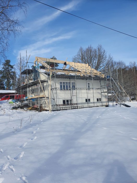 Hus under renovering med ställningar och skenande tak i vintersnö.