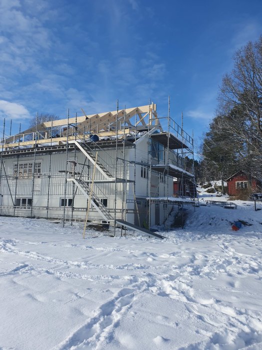 Hus under renovering med byggnadsställningar på vintern med snö runtomkring.