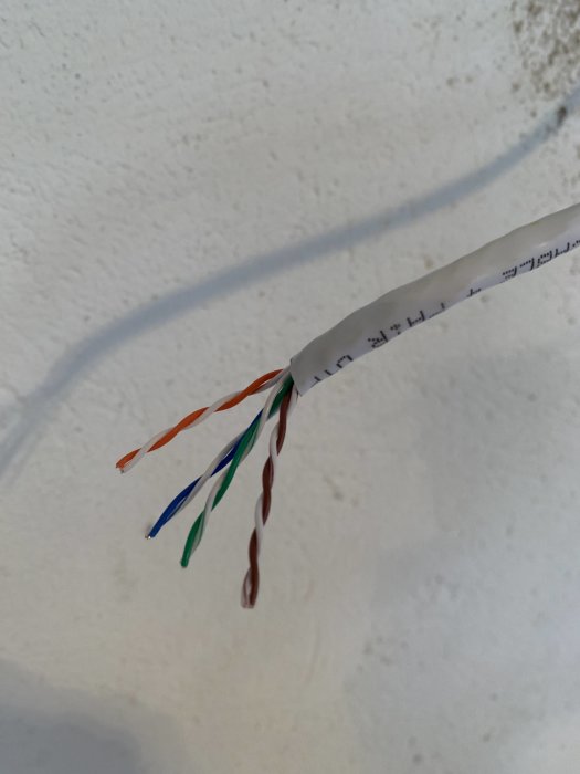 Avskalade ändar av en Ethernet-kabel med exponerade färgkodade trådar mot en vit vägg.