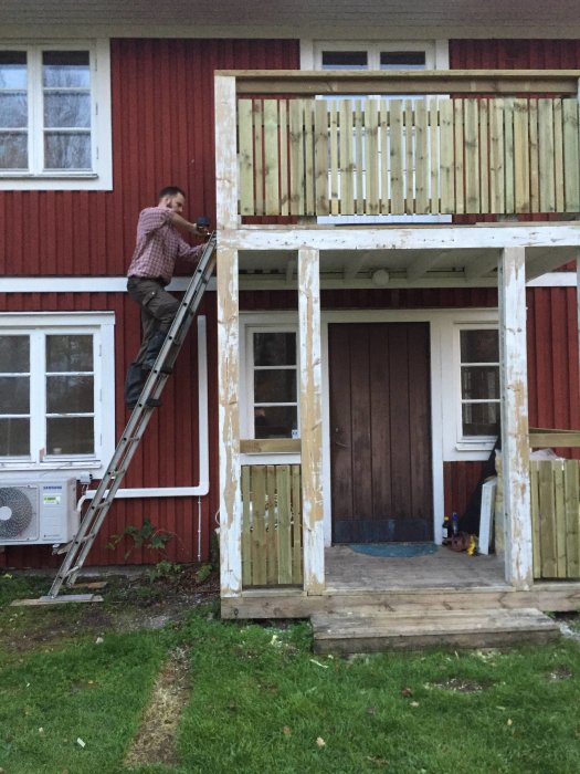 Person på stege som arbetar med att renovera staket på veranda till rött hus.