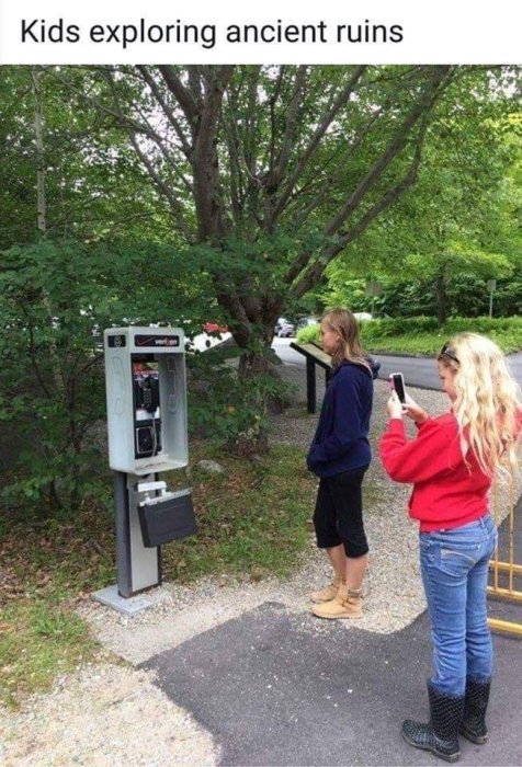 Två unga personer tittar på en offentlig telefonkiosk utomhus.