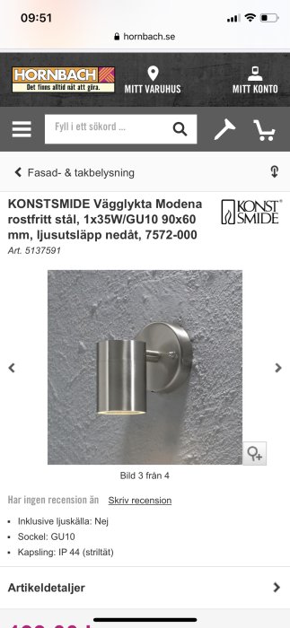 Smal silverfärgad väggspotlight monterad på texturerad vägg med ljuset riktat nedåt.