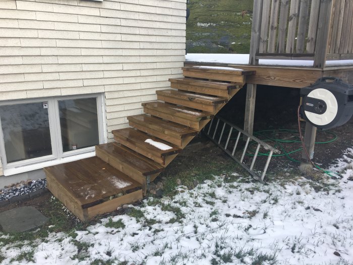 Trappa av vagnstycken utan räcke mot husväggen med snöfläckar på marken.