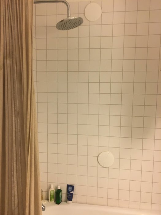 Renoverat badrum med dusch, vita kakelväggar, avtagbart tillufts-don och badrumsprodukter, ingen silikon eller våtspärr synlig.