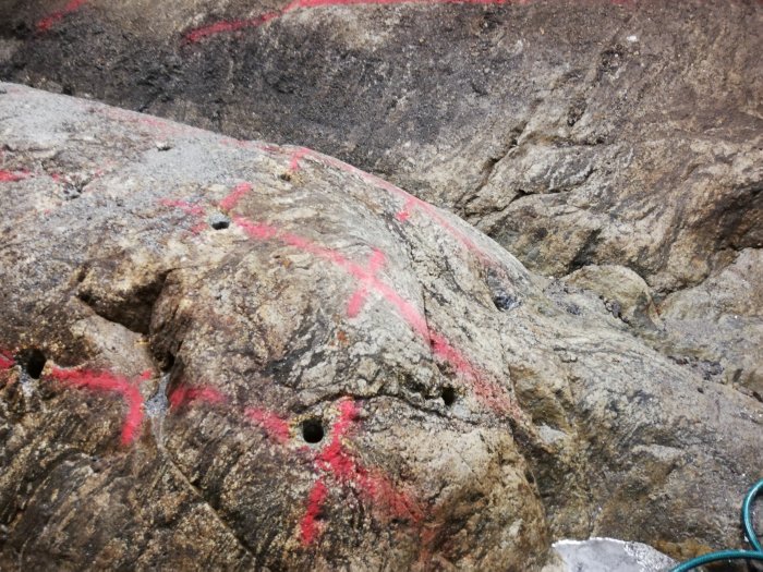 Bergvägg med röd sprayfärg och borrade hål, troligen för bergssäkring eller klättring.