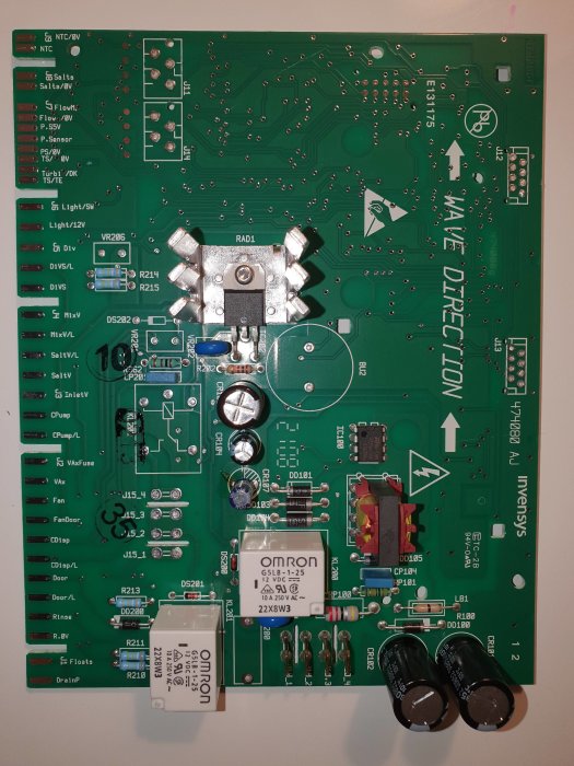 Grönt kretskort med elektroniska komponenter, en del märkningar synliga och en mindre skada på en krets.