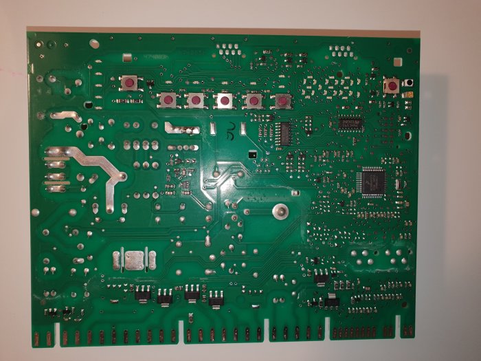 Elektroniskt kretskort med många lödpunkter, komponenter och en skadad IC-krets.