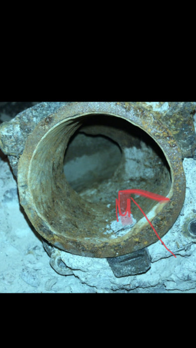 Rostigt rör med synlig skarv markerad av en röd pil som pekar på potentiell vattenläcka.