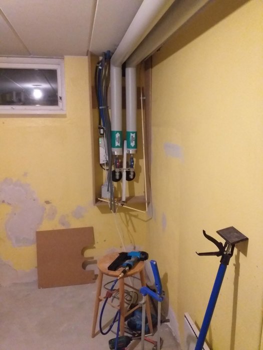 Renovering i källare med exponerade rör, ledningar och verktyg, och en delvis avslagen vägg.