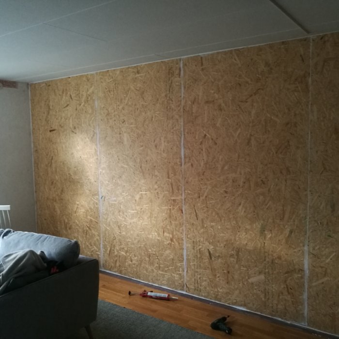 Vägg klädd med OSB-skivor över dubbelgips, förberedd för ytterligare gipsning i ljudisoleringssyfte.