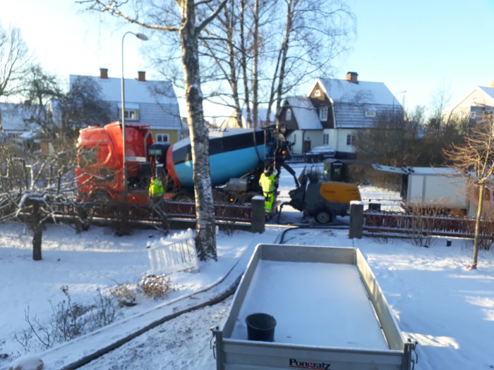 Betongbil och arbetare på plats vid en gjutning i vinterlandskap, mobil pump på släp syns också.