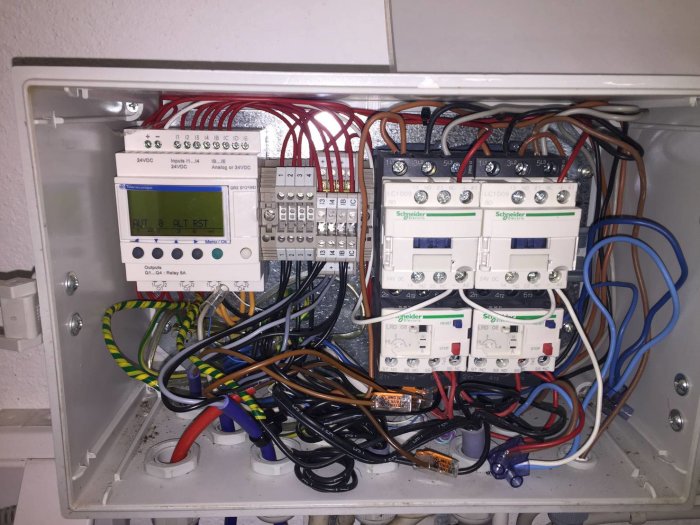 Ett öppet elektronikskåp med trassel av kablar och flera installerade komponenter, inklusive reläer och kretsbrytare.