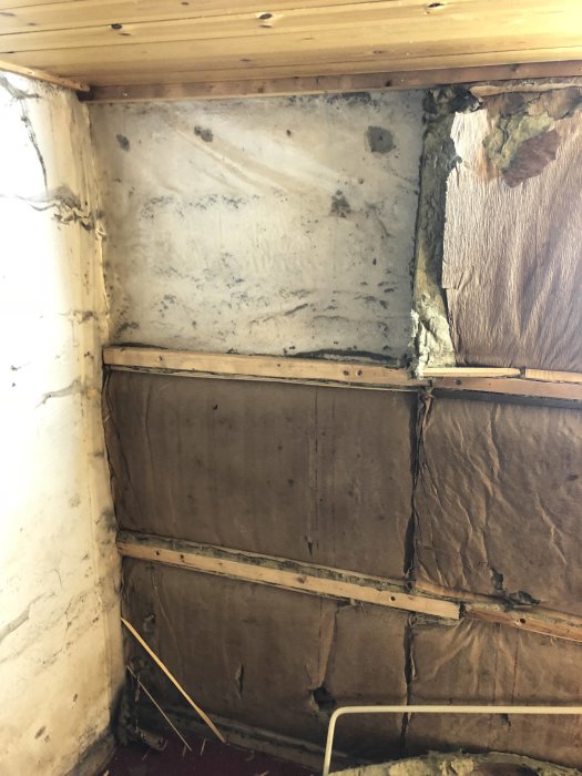 Del av ett källarrum under renovering med synliga isoleringsmaterial, oputsade väggar och träreglar.