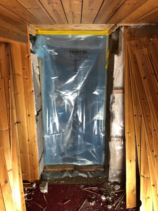 Plastöverdragen dörröppning i ett pågående källarrenoveringsprojekt med synliga träreglar och rivet tak.