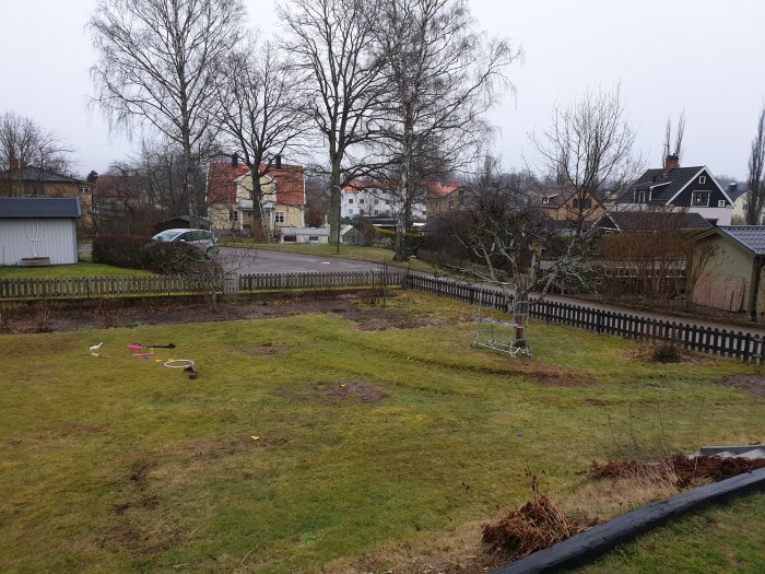 Utsikt över en trädgård med staket och grannarnas parkering, möjlig plats för planterad häck.