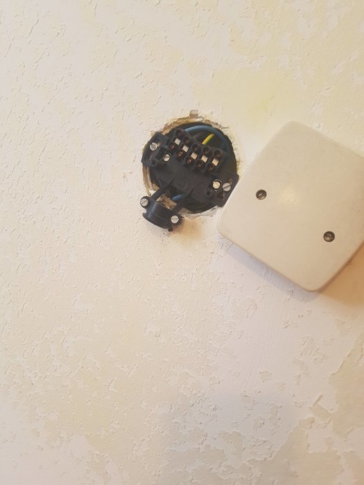 Öppen elektrisk kopplingsdosa i vägg med synliga kablar och en avtagen ljusbrytare bredvid.