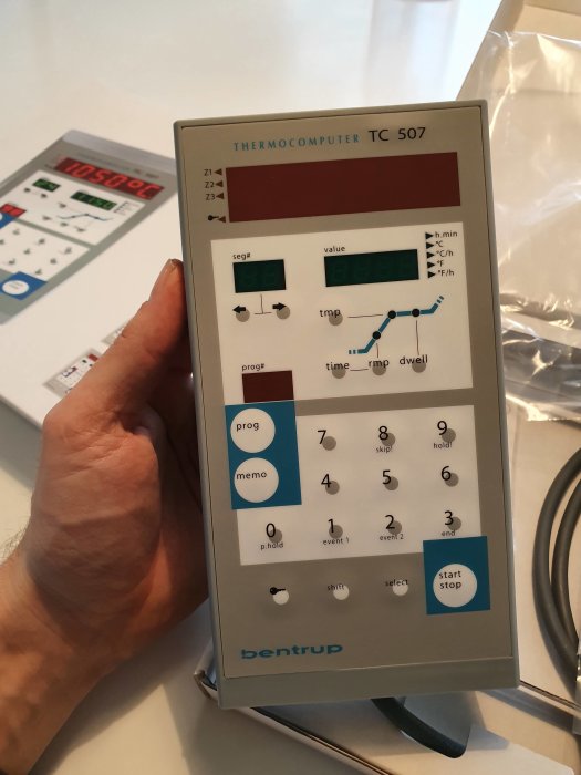 Hand håller en Bentrup TC 507 termocomputer för ugnsautomatik med display och knappar.