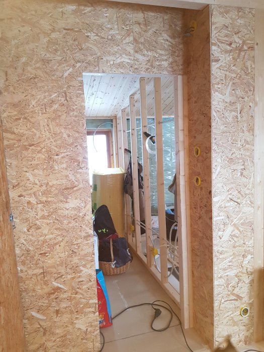 OSB-skivor (oriented strand board) som täcker vägg och dörröppning i ett pågående byggprojekt med synliga timrar och isolering.