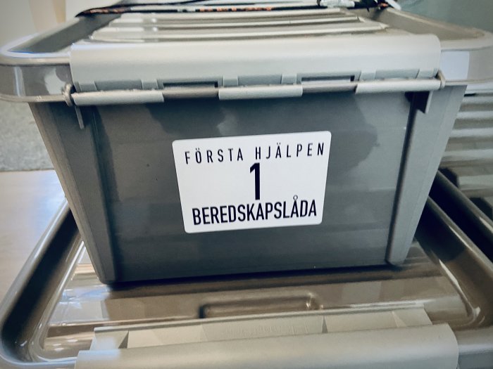 Stapel av gråa förvaringslådor med texten ”FÖRSTA HJÄLPEN 1 BEREDSKAPSLÅDA”.