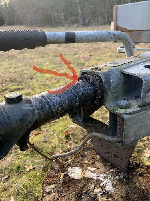 Nahaufnahme einer Anhängerkupplung mit Spiel an der Zugstange, markiert mit einem roten Pfeil, auf einem alten Anhänger.