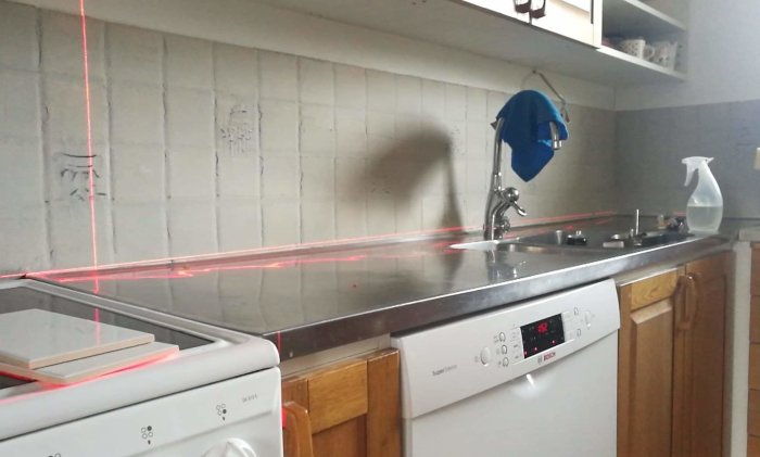 Kök med diskbänk och tvättmaskin där en laser visar ojämnheter i väggens kakel.