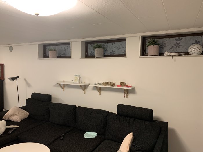 Renoverad källare med svart soffa, hyllor på väggen och små fönster med gardiner.