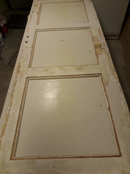 En gammal vit masonitklädd spegeldörr liggande ned, med delvis borttagna kvartsstavar och masonit insatt i speglarna.