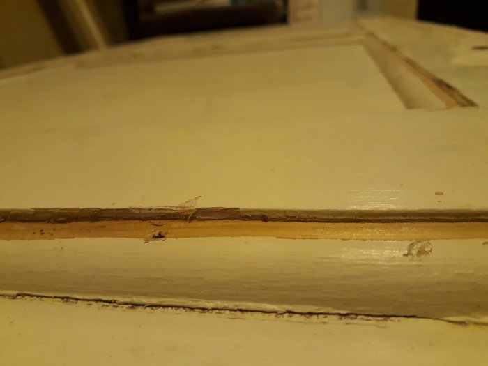 Närplan av en vit spegeldörr med synlig skada där kvartsstavar hyvlats bort och masonit skynker utrymmet.