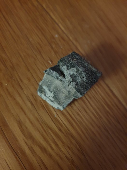 Bit av grönt, sprött material som liknar avjämningsmassa, funnet under tröskel på ett trägolv.