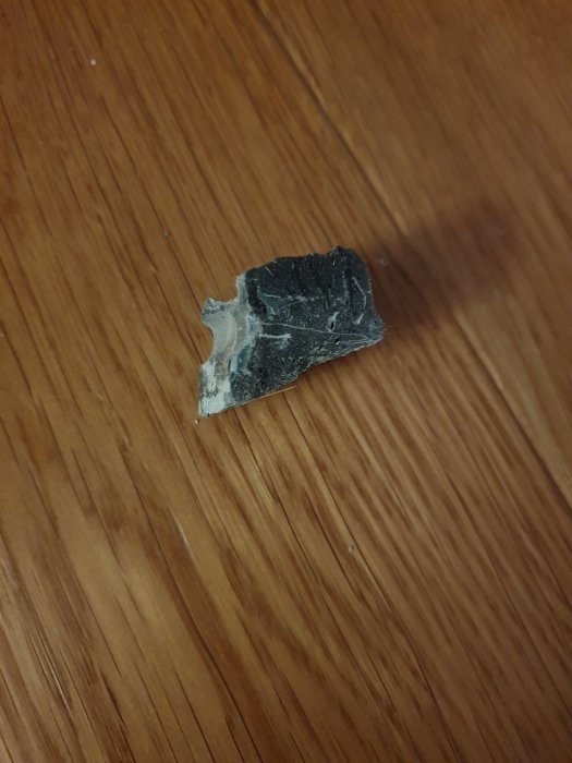 Bit av grönt, sprött material på trägolv som kan vara gammal avjämningsmassa under tröskel.
