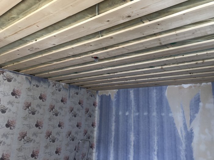 Wooden ceiling beams installed 30cm apart with partially removed wallpaper on walls in a renovation project.