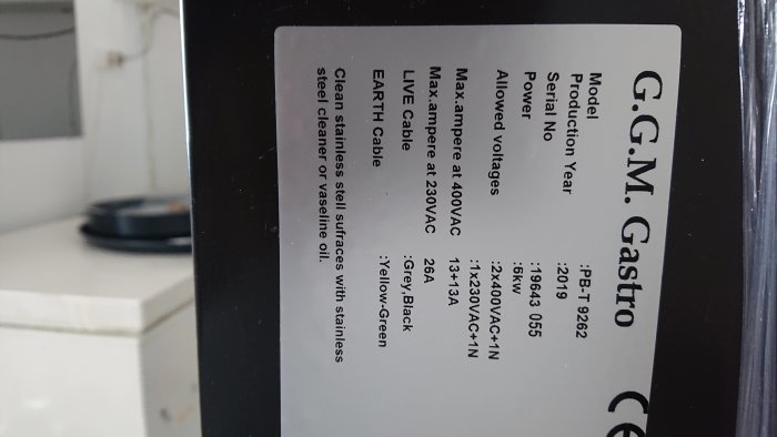 Typskylt på en apparat med teknisk information om modell, serienummer, spänningar och kabelfärger.