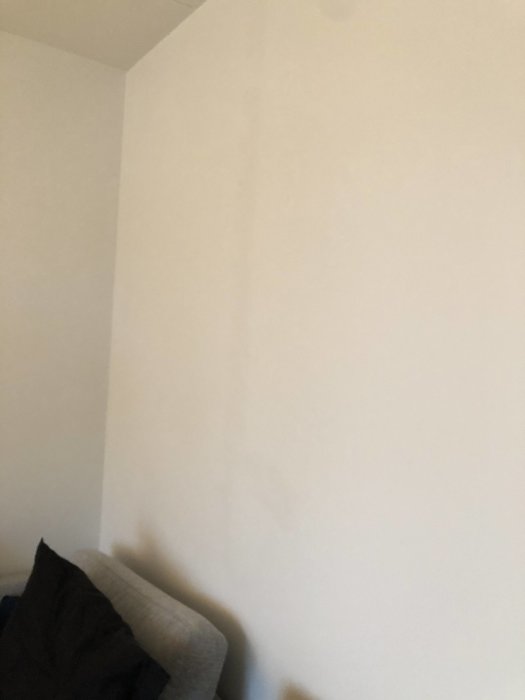 En vit målad vägg med synliga vertikala sprickor där ny mälarfärg inte döljer sprickorna helt.