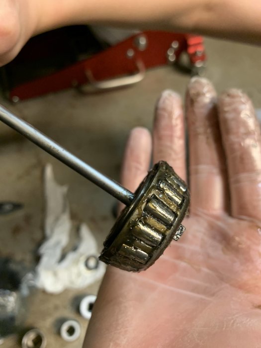 Hand håller ett smutsigt hjullager med verktygsbakgrund, som troligen behöver bytas på släpkärra.