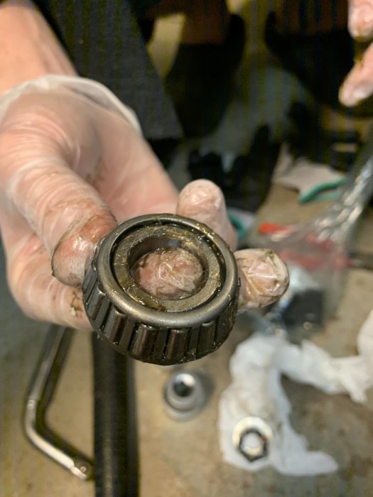Närbild av ett smutsigt hjullager hållet i en hand, verktyg och trasor i bakgrunden.