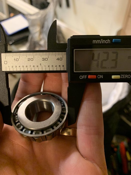 Skjutmått som mäter diameter på en rengjord kullager på 42,3 mm i en person hand.