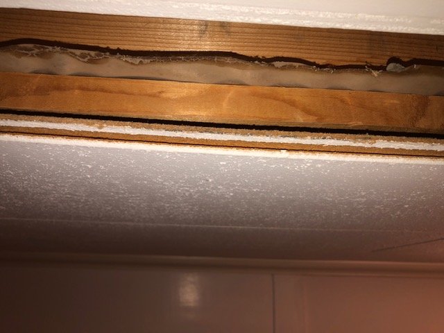 Inblick i takets struktur vid en öppning, visar spånskiva och träbjälkar, möjlig fästpunkt för akvariearmatur.