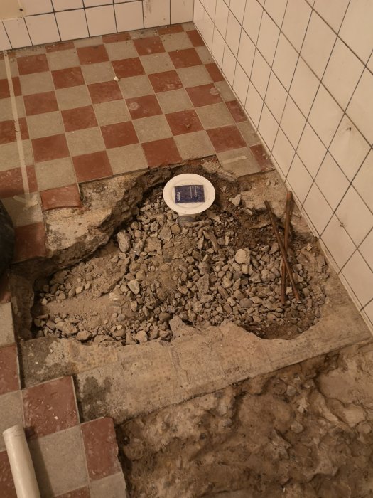 Nyinstallerad purusbrunn i källare med omgivande rörliga grus och betongrester samt klinkergolv och kakelväggar.