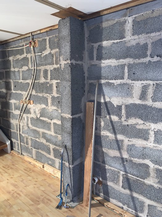 Pelare i källare med reglad vägg, kablar och rör, samt verktyg och trägolv.