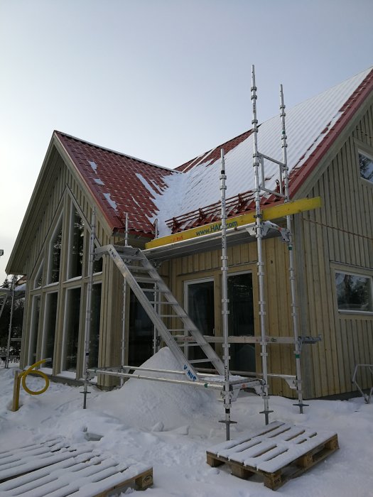 Ett hus under uppbyggnad med stomme och tak, omgivet av ställningar och snötäckt mark.