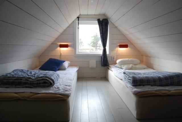 Loftet med Gotlandspanel, to enkeltsenge ved siden af hinanden, vindue imellem dem, simple røde væglamper på hver side.