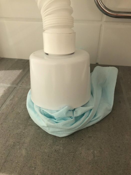 Tillfällig anslutning av avloppsrör med plastkopp och handduk på badrumsgolv.