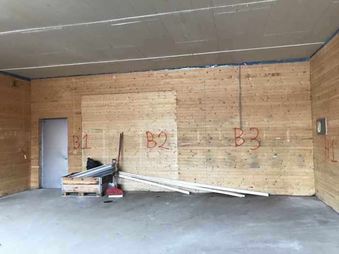 Inredning av garage förberedd för rivning, markerade sektioner B1, B2, B3 på träväggen och liggande byggmaterial.