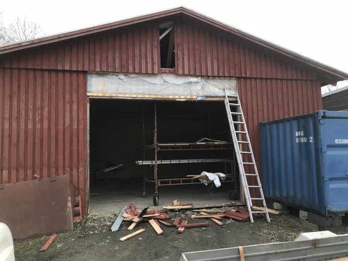 Lada med borttagen vägg och port inför renovering, byggnadsställning och byggavfall syns.