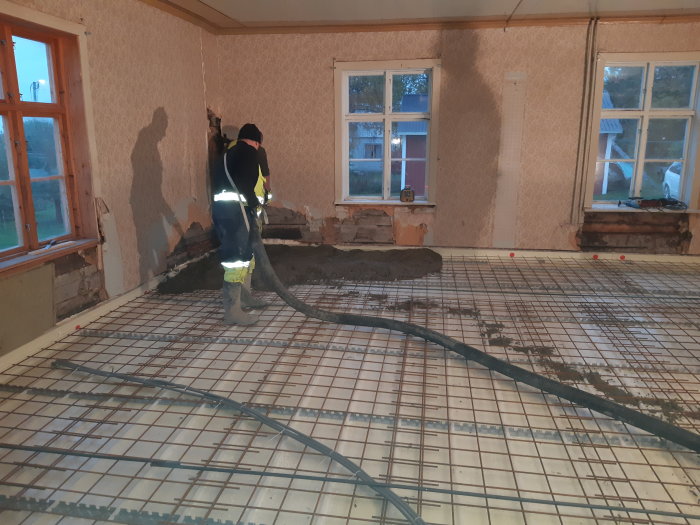 Arbetare häller betong över armeringsnät på ett golv i ett under renovering.